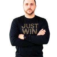 A man with short hair and a beard stands with arms crossed, wearing a black long-sleeve shirt that says JUST WIN in gold letters. The background is white. JW Training and Development